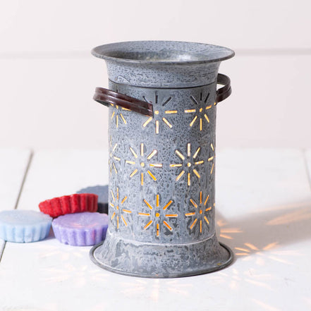 Weathered gray cylindrical metal wax warmer with starburst cutouts and wooden side handles, casting star-shaped shadows beside colorful wax melts.
