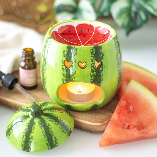 Glossy green ceramic watermelon warmer with red seeded basin and three heart-shaped cutouts lit by a tealight; matching lid.