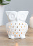 White glossy ceramic owl wax warmer with teardrop cutouts glowing from a lit tealight.