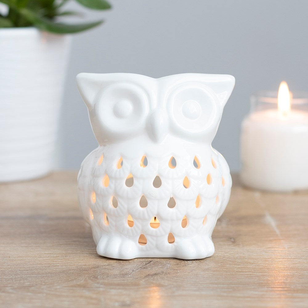 White glossy ceramic owl wax warmer with teardrop cutouts glowing from a lit tealight.