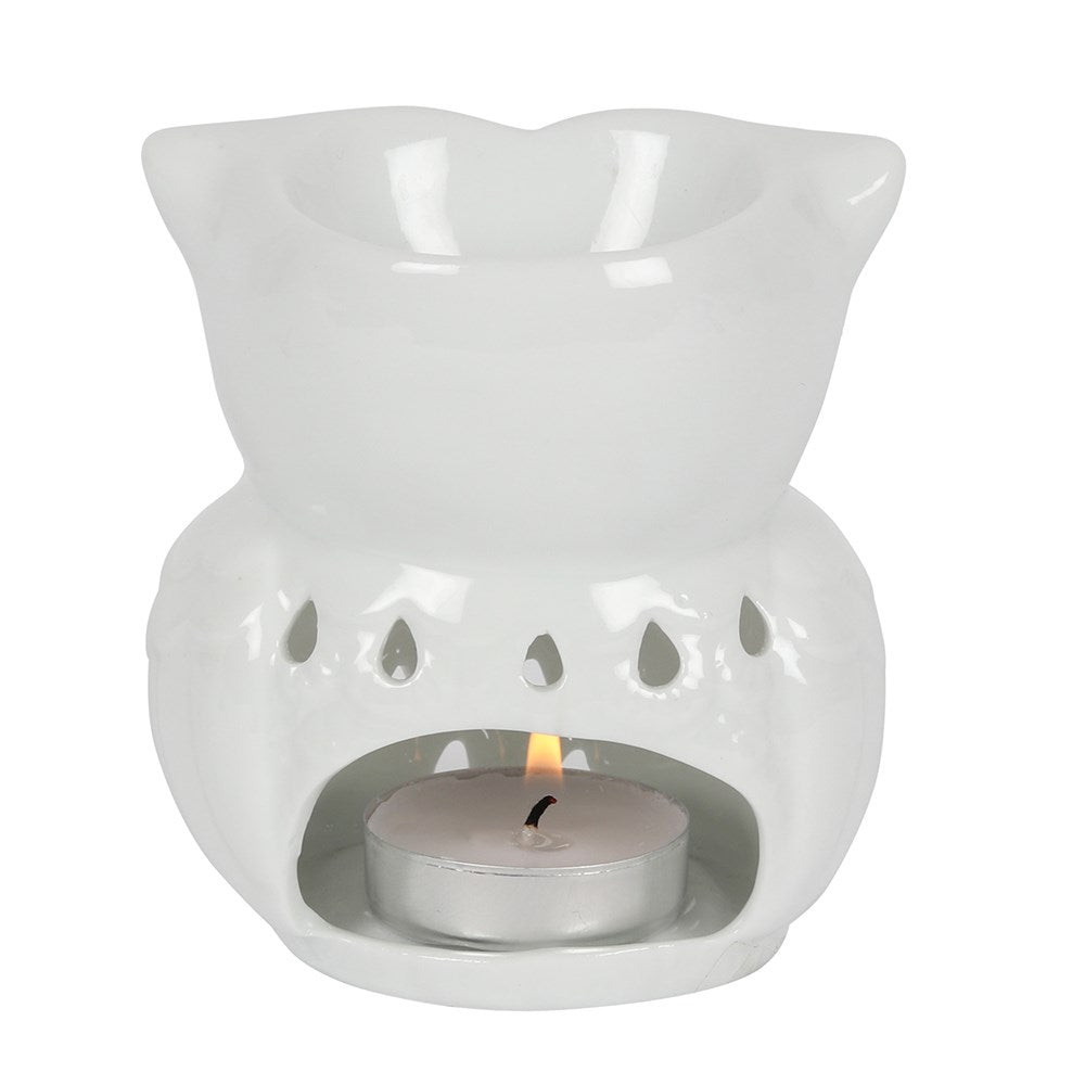 White ceramic owl-shaped wax warmer with top bowl, teardrop cutouts and a lit silver tealight in the front cavity on a white background.