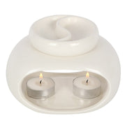 White glossy ceramic double oil burner/wax warmer with a divided round top dish and two lit tealights in metal cups inside an arched front cavity