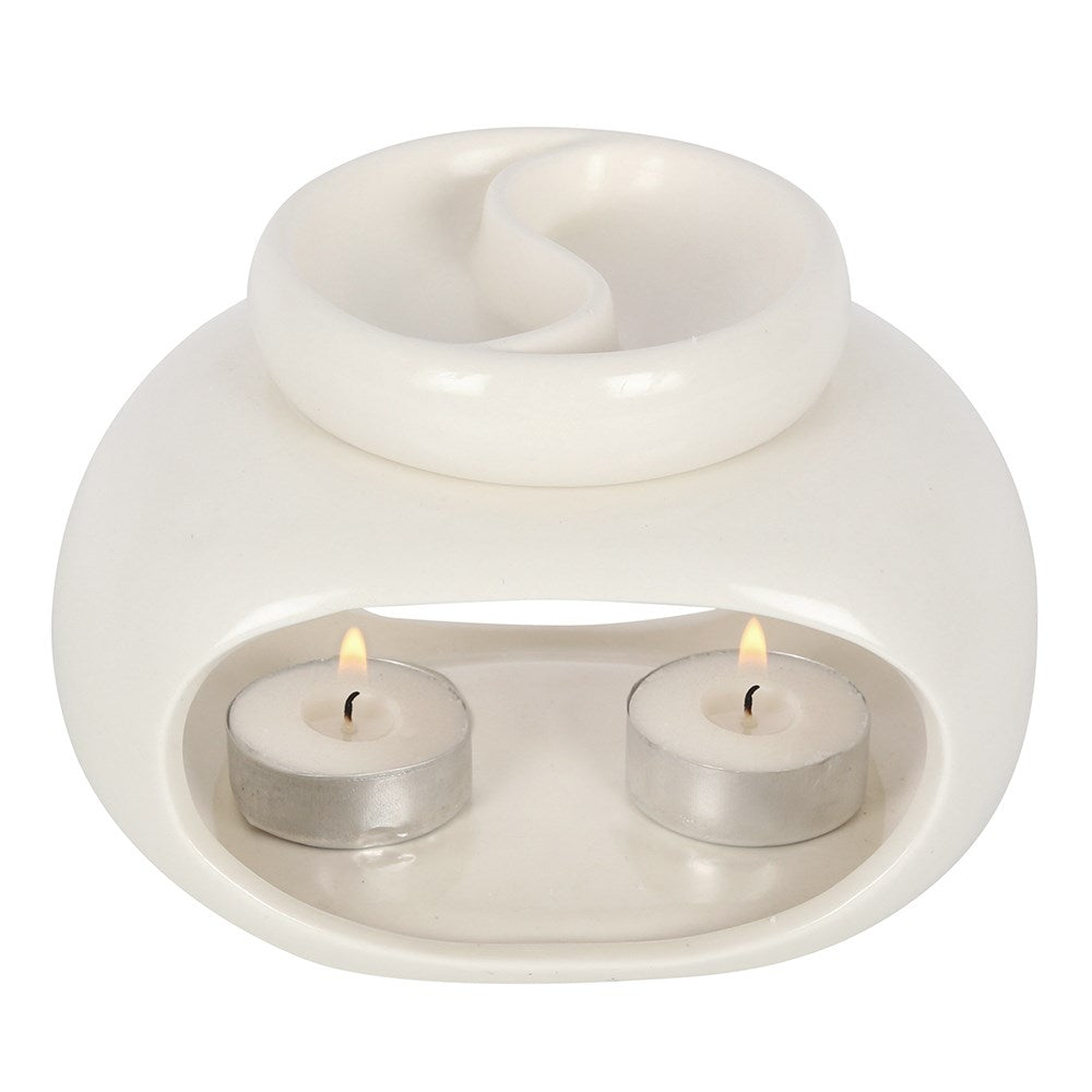 White glossy ceramic double oil burner/wax warmer with a divided round top dish and two lit tealights in metal cups inside an arched front cavity