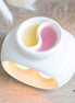 White glossy ceramic double-bowl warmer with yin-yang divider holding yellow and pink melted wax.