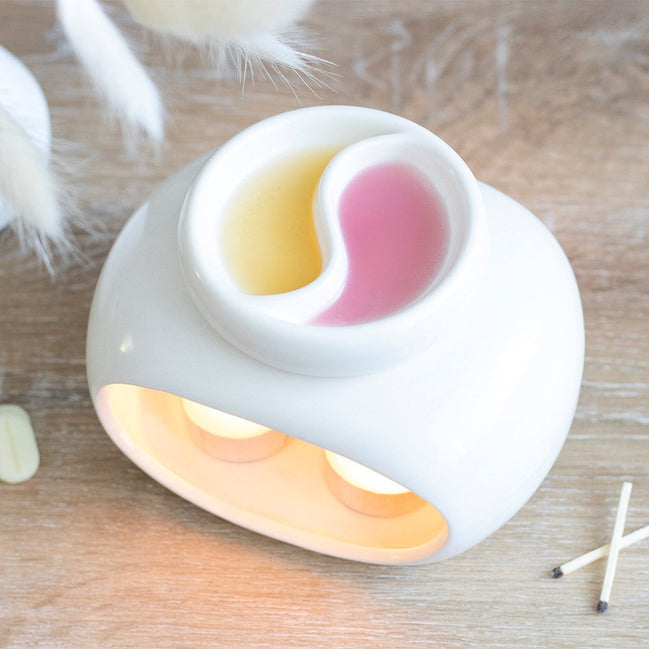 White glossy ceramic double-bowl warmer with yin-yang divider holding yellow and pink melted wax.